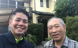 若い男性と高齢の男性が屋外で笑顔を見せているツーショット